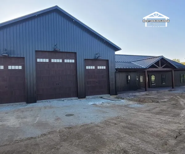Modern two-story barndominium with dark grey siding, a metal roof, and a large wraparound porch.